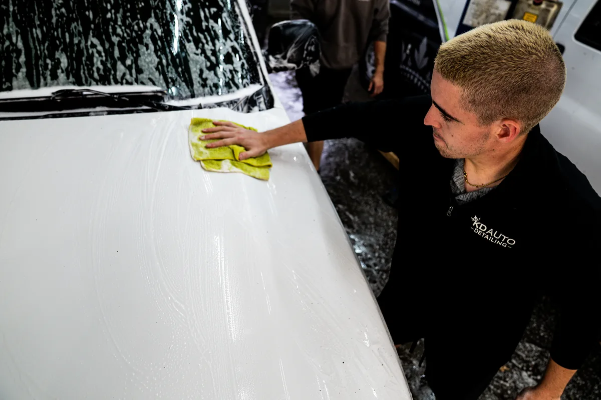 Auto detailer hand-washing a vehicle with a microfiber mitt