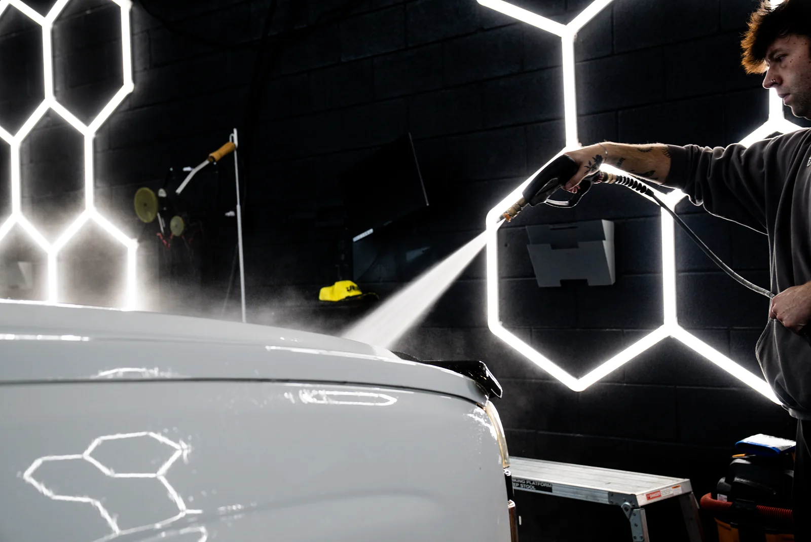 Detailer pressure-washing a pickup truck inside an auto detailing shop